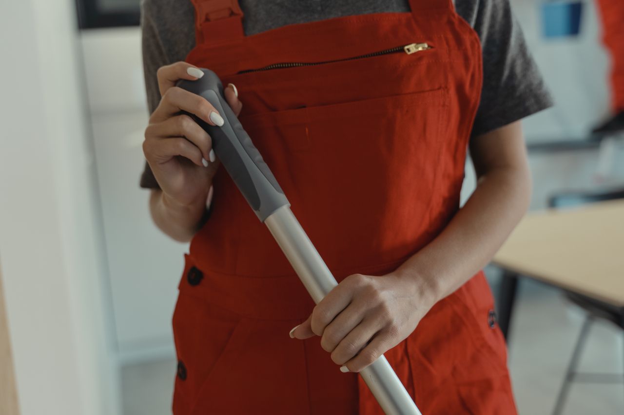A woman wearing a red apron is holding a mop handle while cleaning indoors.